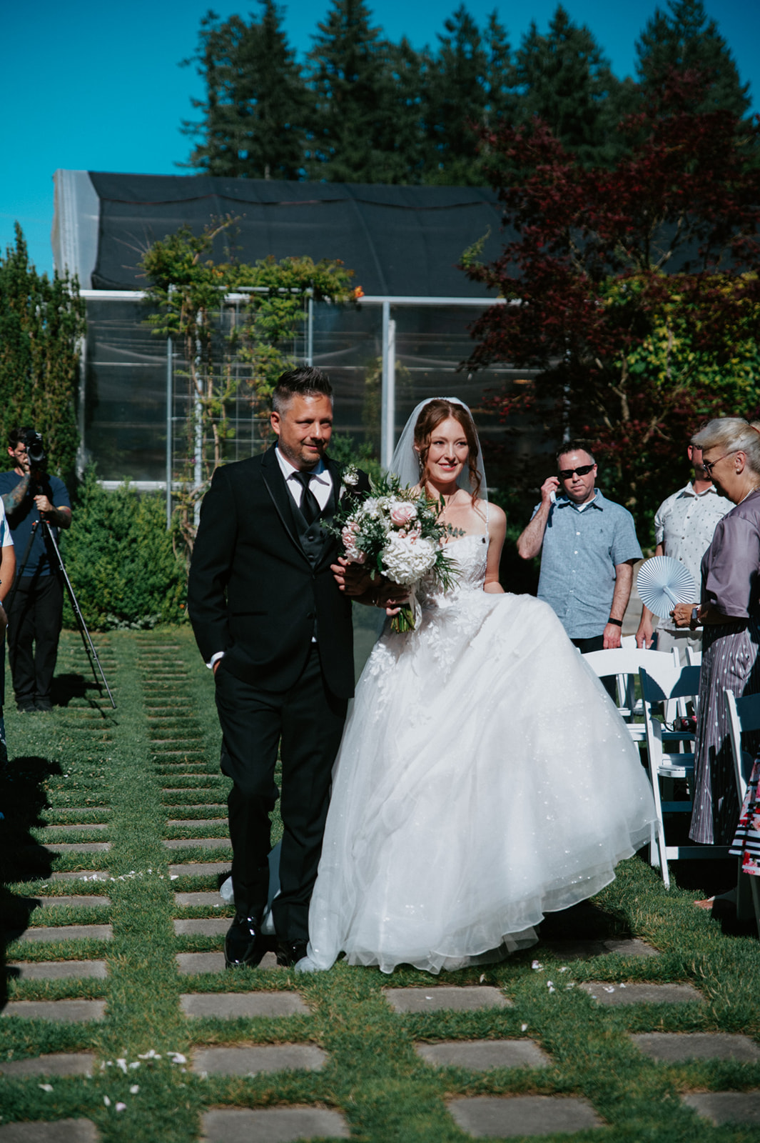 Bride walking down a garden aisle with a man in a black suit while carrying a floral bouquet at her wedding in seattle.