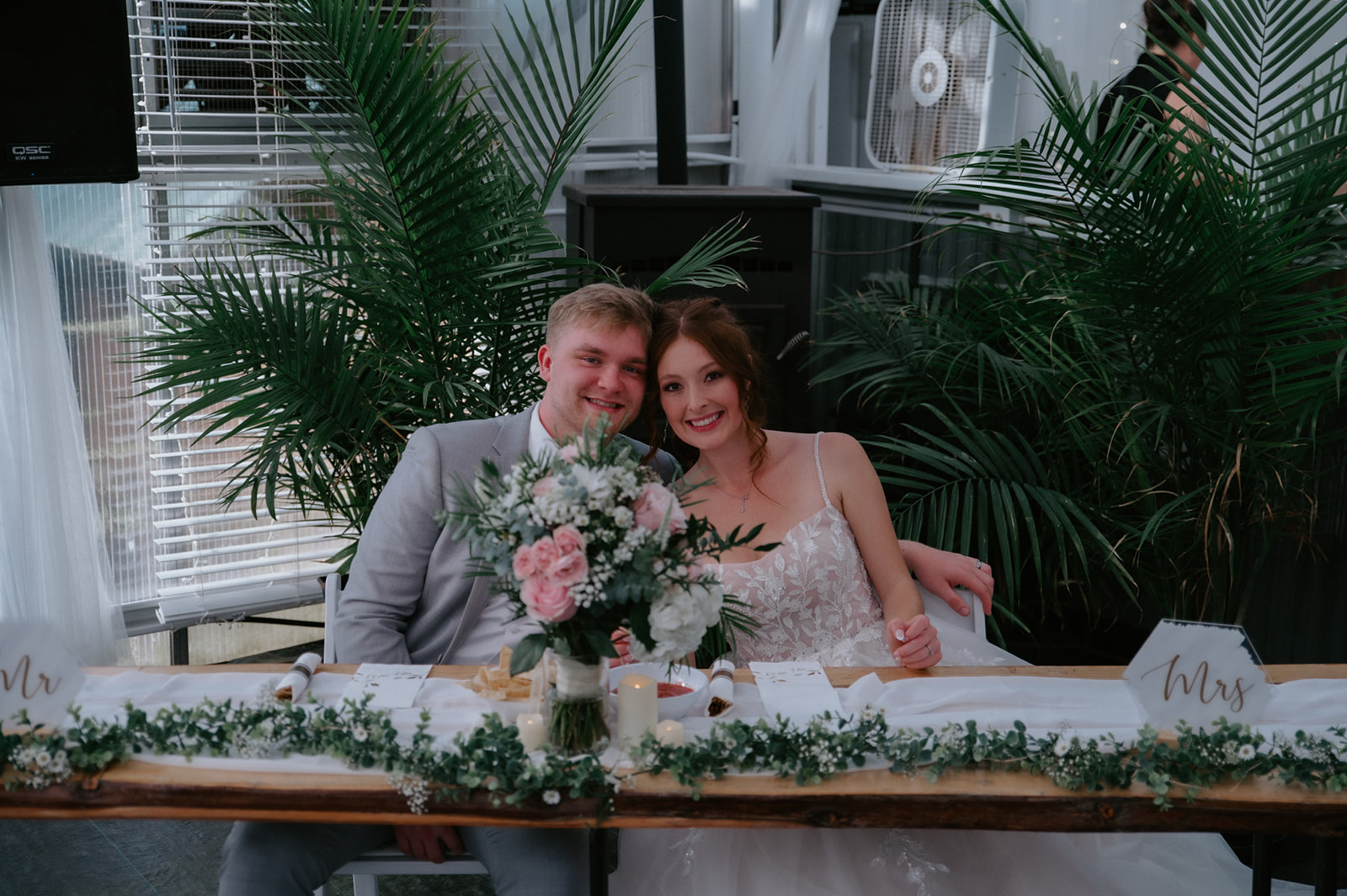 Bride and groom smiling at their sweetheart table decorated with pink flowers and greenery during their wedding in seattle.