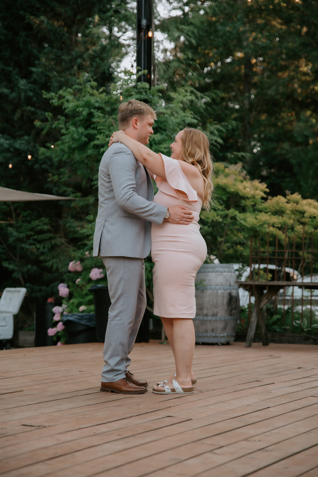 Man in a light gray suit dancing with a woman in a blush pink dress at an outdoor celebration.