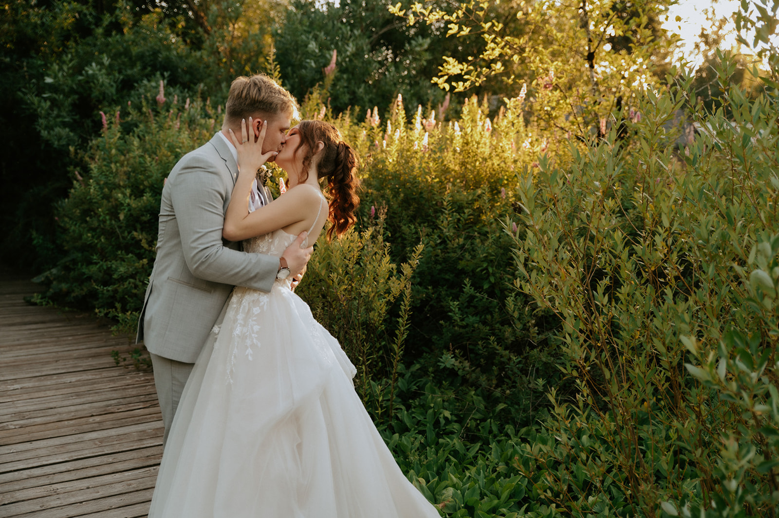 Newlyweds kissing beside a wooden garden walkway surrounded by wildflowers during their wedding in seattle.