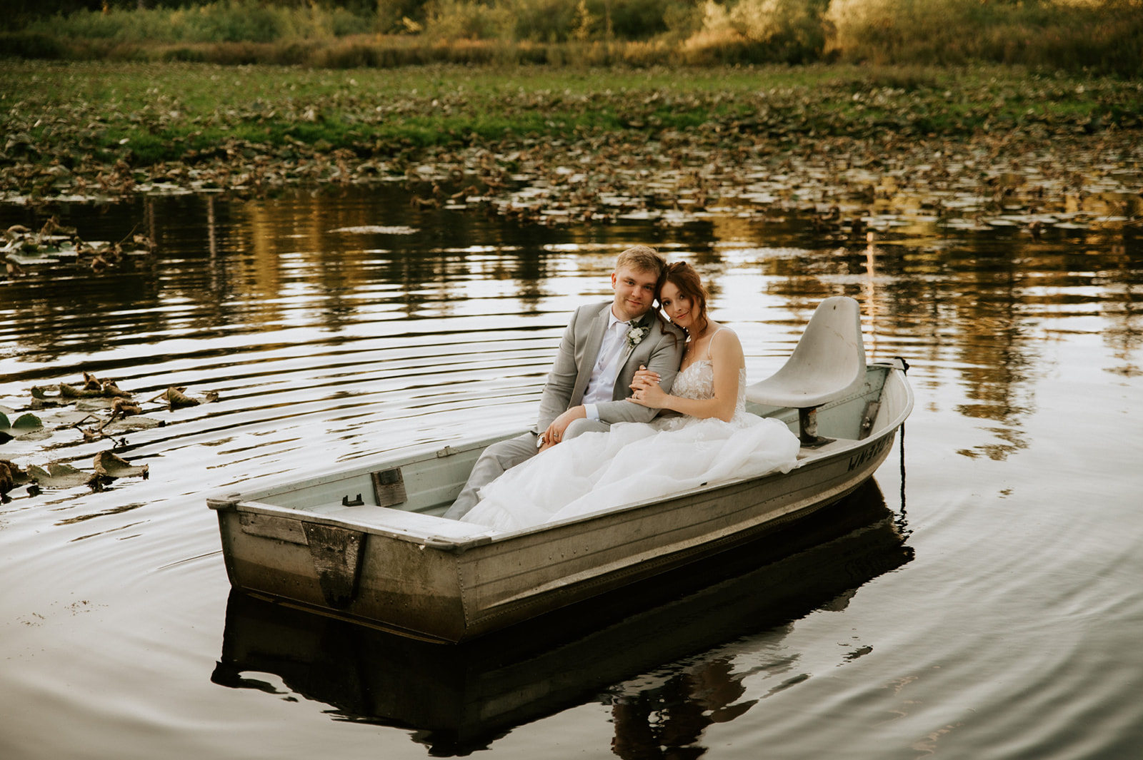Bride and groom cuddling in a small boat surrounded by golden reflections on the water after their wedding in seattle.