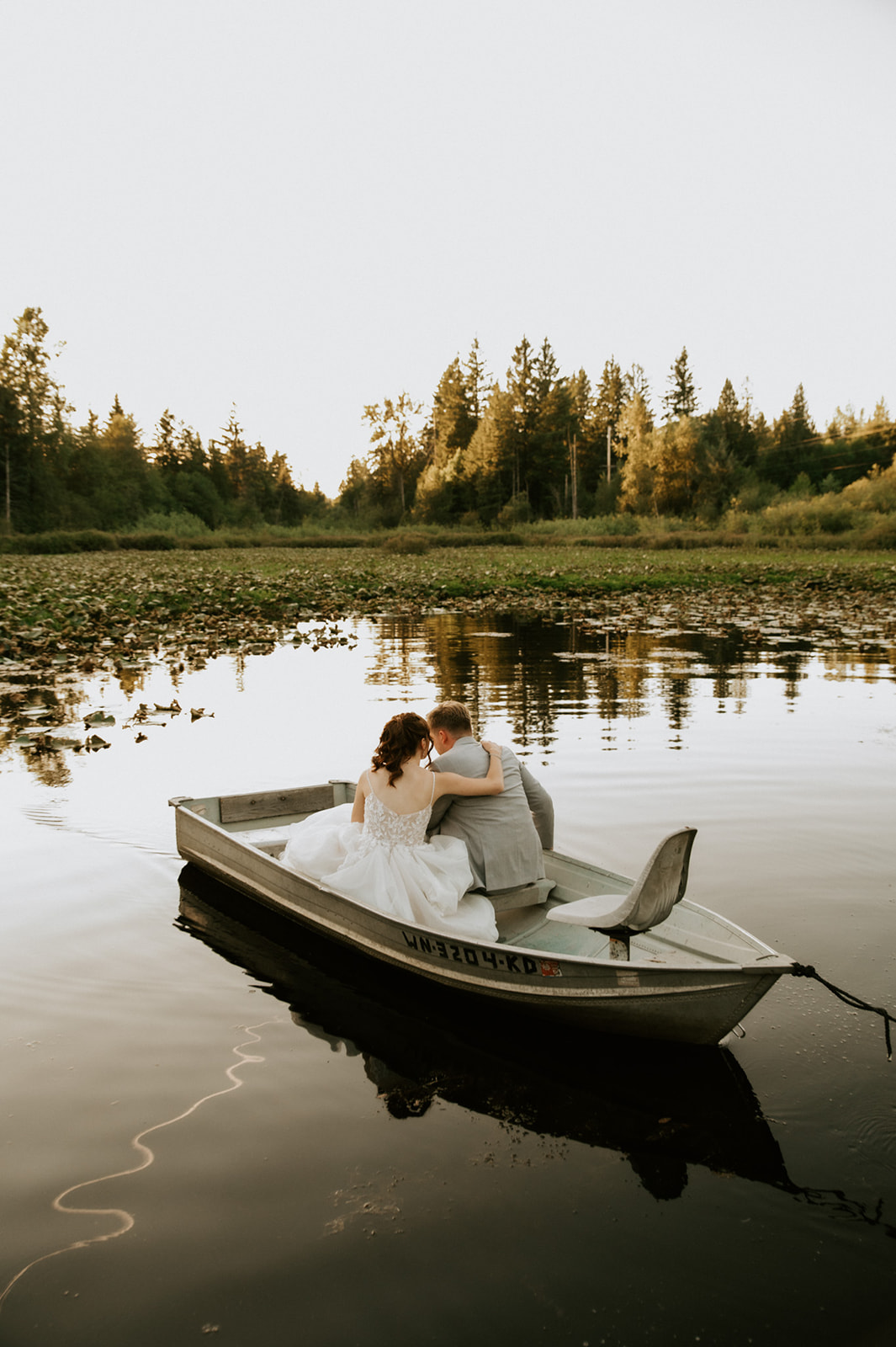 Bride and groom cuddling in a small rowboat on a peaceful pond surrounded by trees after their wedding in seattle.