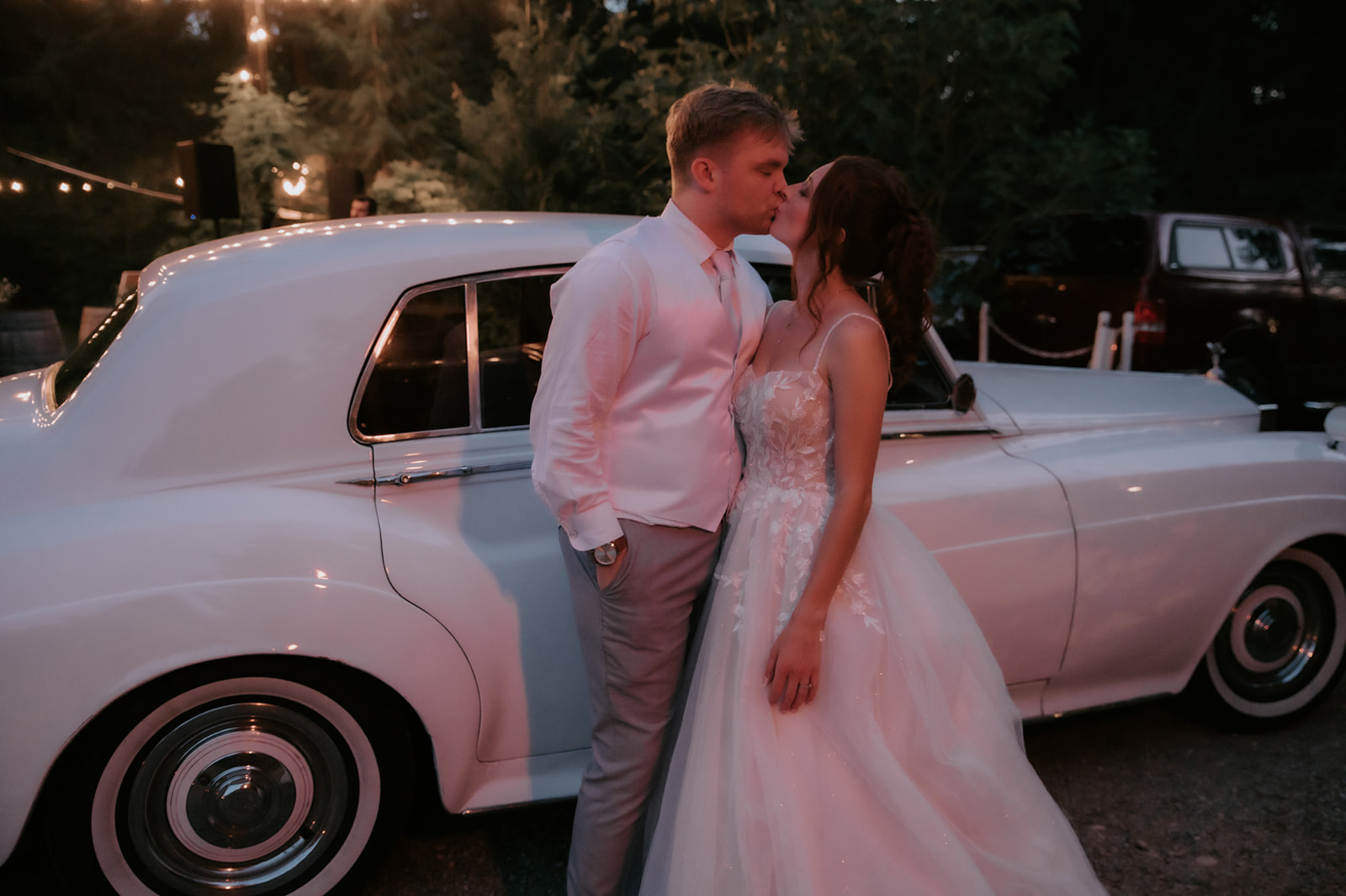 Newlyweds sharing a kiss beside a vintage white car at dusk after their wedding in seattle.